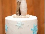 a white wedding cake with black ribbon and blue sugar snowflakes plus a couple topper