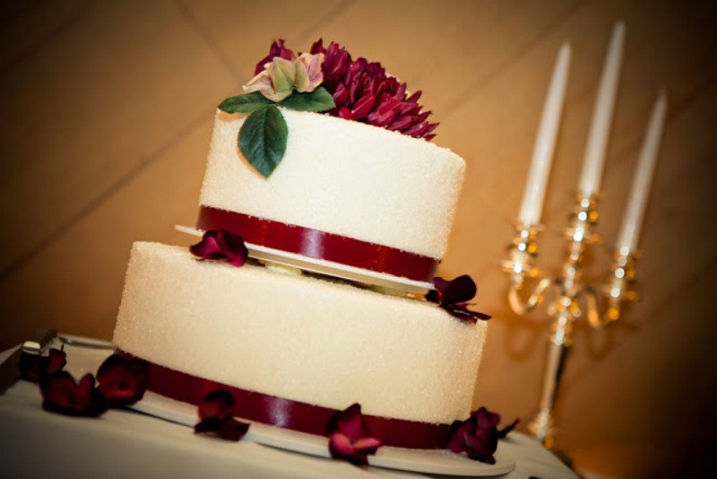 A classic white wedding cake with burgundy ribbon and burgundy blooms and greenery on top is a bold and cool idea