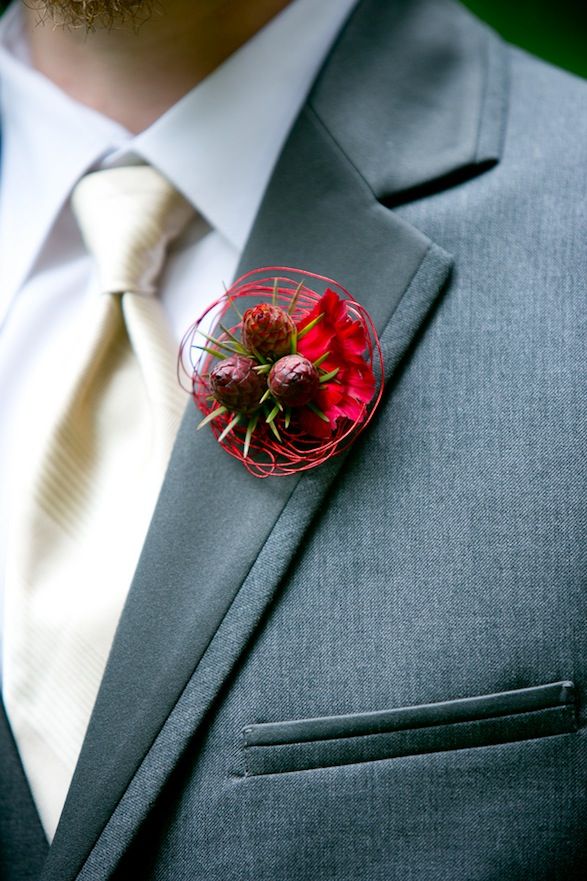 A bright red boutonniere of petals, blooms and some red vine is a bold accent for a winter groom's look
