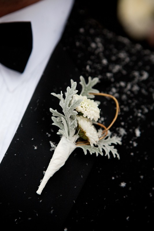 A pale boutonniere of white blooms and pale leaves for accessorizing a classic and chic groom's look