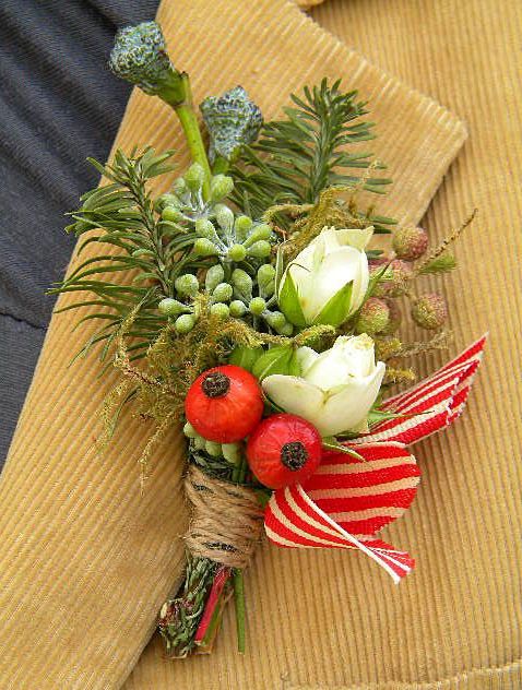 a bright boutonniere of red and white striped ribbons, berries, white blooms and greenery plus succulents for a winter groom