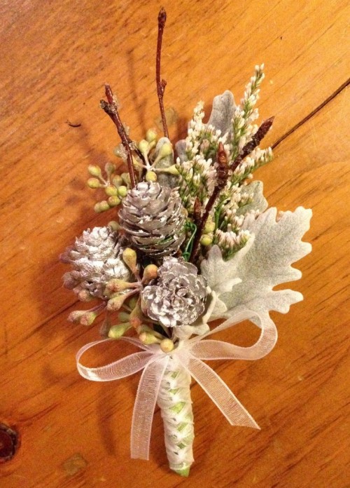 a pale winter wedding boutonniere with snowy pinecones, sitcks, berries and pale leaves plus a white ribbon bow