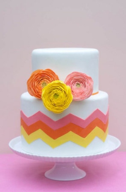 a white wedding cake decorated with pink, coral and yellow chevrons and matching ranunculus is a lovely idea for a wedding with this color scheme