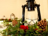 a rustic Christmas wedding centerpiece of greenery, pinecones, red roses and a vintage lamp is chic