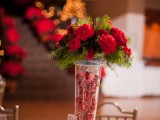 a refined Christmas wedding centerpiece of a tall vase with berries, fir branches and red blooms is very stylish