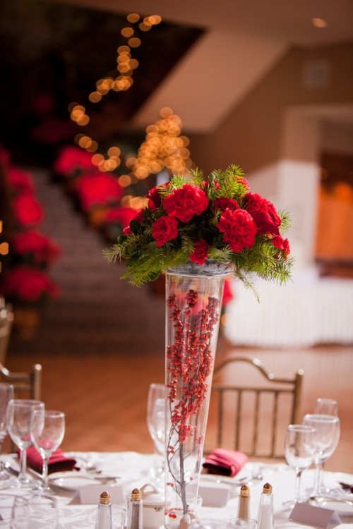 a refined Christmas wedding centerpiece of a tall vase with berries, fir branches and red blooms is very stylish