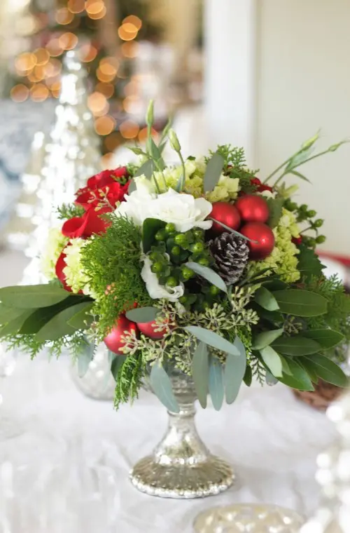 a chic and refined Christmas wedding centerpiece of a silver bowl, white and red blooms, pinecones and greenery is amazing