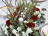 a frozen Christmassy wedding centerpiece of greenery, branches, white and burgundy blooms and candles in the center