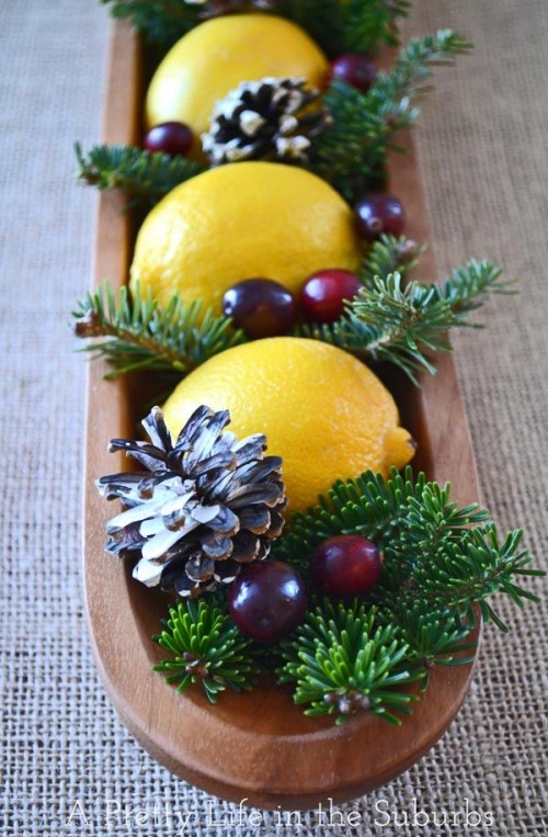 a cozy rustic Christmas wedding centerpiece of a long wooden bowl with pinecones, berries, fir branches and lemons is stunning