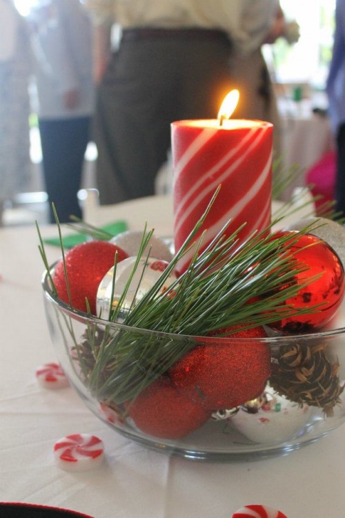 a simple Christmas wedding centerpiece of a wooden bowl with silver and red ornaments, a red candle and fir branches