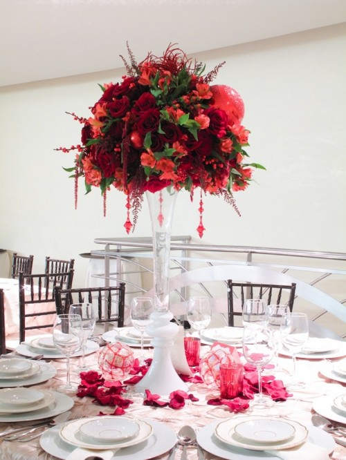 a beautiful whimsical Christmas wedding centerpiece of a tall vase with red and burgundy blooms, greenery and hanging crystals