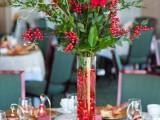 a bold Christmas centerpiece of a tall vase filled with red ornaments, greenery, berries, red roses, twigs is very elegant and chic