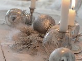 a silver and white Christmas wedding centerpiece of shiny and glitter ornaments, candles in candleholders and feathers