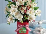 a chic and bold Christmas wedding centerpiece of a red jar, white blooms and red berries and a red striped bow and a card on the vase