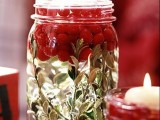a jar with greenery, floating berries and a floating candle is a bold idea for a Christmas wedding, make as many as you want