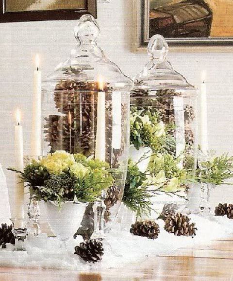a refined Christmas wedding centerpiece of tall glass jars filled with pinecones, greenery and white blooms in bowls and pinecones on the table