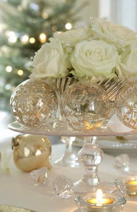 a refined Christmas wedding centerpiece of a glass stand, shiny metallic ornaments and white roses in a foil bowl is very chic