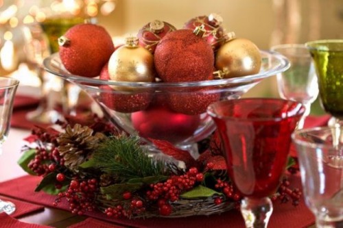 a Christmas wedding centerpiece of a glass bowl filled with burgundy and bold ornaments, with fir branches, berries and pinecones around