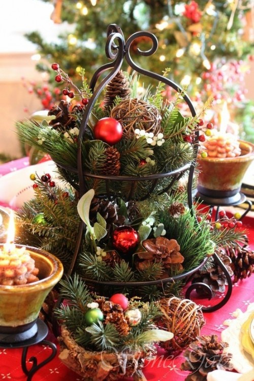 a tiered metal stand with fir branches, pinecones, vine balls, berries and red Christmas ornaments is great for a rustic wedding