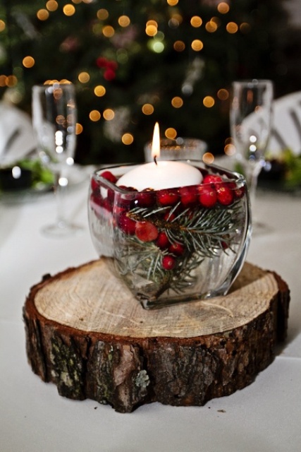 a rustic Christmas wedding centerpiece of a glass bowl with floating fir branches, berries and a candle placed on a wood slice