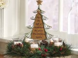 a Christmas wedding centerpiece of a fir wreath, berries, candles and with a metal sign fir tree in the center