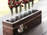a rustic Christmas wedding centerpiece of a wooden box with bells, bottles with fir branches, pinecones and berries for a rustic celebration