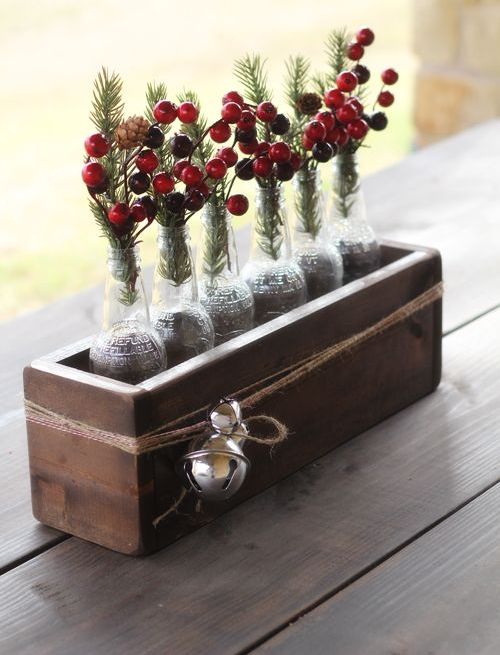 a rustic Christmas wedding centerpiece of a wooden box with bells, bottles with fir branches, pinecones and berries for a rustic celebration