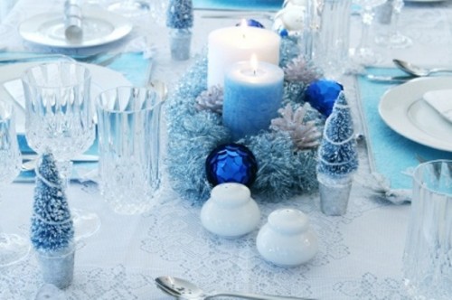 a blue Christmas wedding centerpiece of a frozen wreath with blue ornaments, candles, mini fir trees and sparkles all around