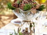 a rustic Christmas wedding centerpiece of a crystal bowl, pinecones and fir branches plus some fir in a glass next to it will bring a rustic feel