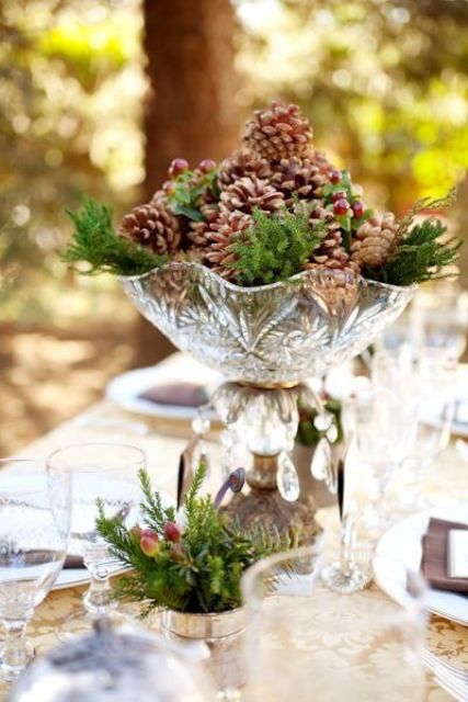 a rustic Christmas wedding centerpiece of a crystal bowl, pinecones and fir branches plus some fir in a glass next to it will bring a rustic feel