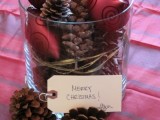 a cozy rustic Christmas centerpiece of a glass vase filled with red ornaments and pinecones plus a tag is a cool idea to rock