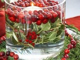 an oversized glass bowl with greenery, cranberries and floating candles and the same on the table is very Christmassy