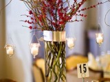 a Christmas wedding centerpiece of a tall vase, branches with berries, hanging candles and a table number is cool and easy