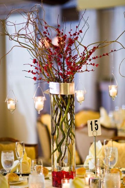 a Christmas wedding centerpiece of a tall vase, branches with berries, hanging candles and a table number is cool and easy