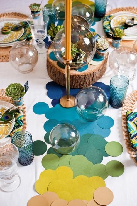 a bright blue, green, yellow, tan paper circles, succulents and moss, peacock feathers, a wood slice and yellow candles in gold candlesticks