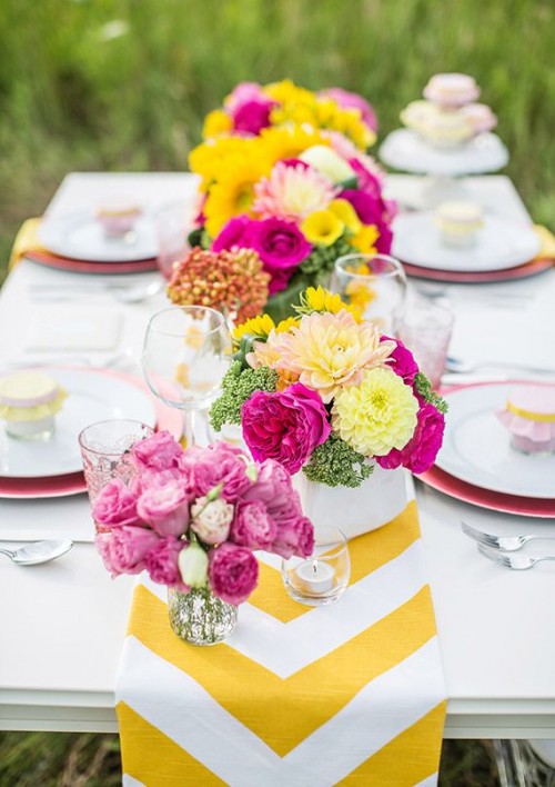 a cheerful and colorful wedding tablescape with a yellow chevron runner, yellow and hot pink blooms, pink plates and yellow napkins is a lovely idea