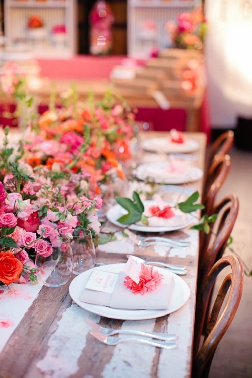 a colorful wedding tablescape with pink, orange and red blooms and greenery, neutral napkins and red blooms and greenery is a lovely idea
