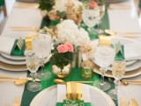a bright and elegant wedding tablescape with an emerald table runner, napkin rings and cards, with gold favors and cutlery, pink and white blooms and foliage