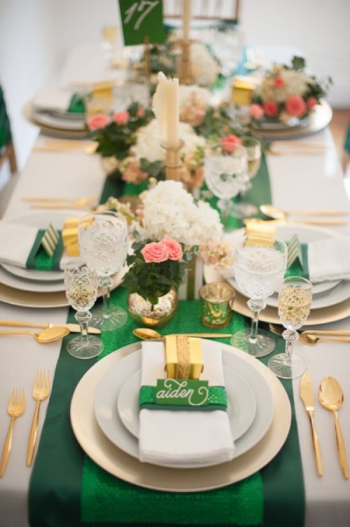 a bright and elegant wedding tablescape with an emerald table runner, napkin rings and cards, with gold favors and cutlery, pink and white blooms and foliage
