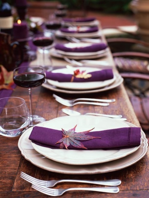 a bold and chic fall wedding tablescape with purple napkins, a table runner and purple candles, fall leaves marking each place setting is amazing