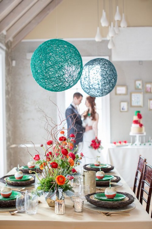 a bright wedding tablescape with green glitter plates, bold red and orange blooms and greenery, turquoise and navy yarn balls over the table
