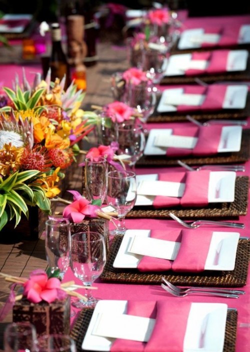 a bright tropical wedding tablescape with pink table runners, napkins and blooms, with a centerpiece of tropical fruit and flowers
