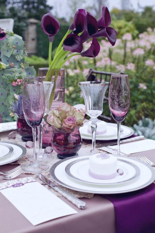 a bold wedding tablescape with a lilac tablecloth, purple napkins, purple glasses and callas, some crystals and a doily