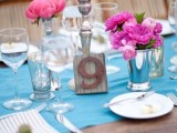 a pretty bright wedding table setting with a blue table runner, pink and hot pink blooms, candles and white porcelain and napkins