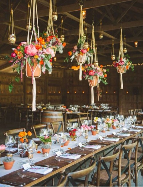 a pretty boho wedding tablescape with super bright blooms, red, orange and pink ones, greenery and succulents and hanging arrangements over the table