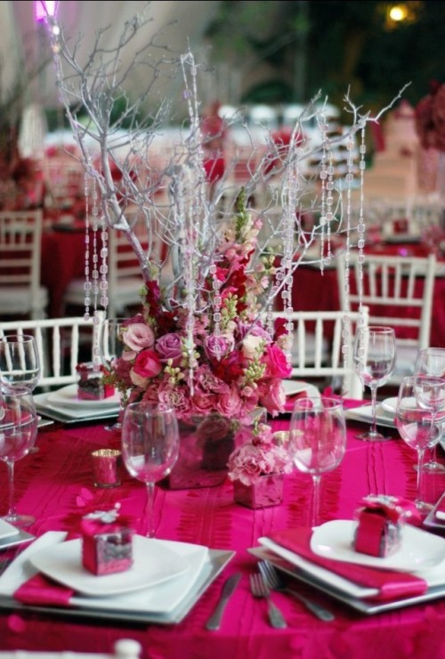 a hot pink wedding tablescape with a bold tablecloth, ribbons, hot pink and pink blooms and silver branches with crystals hanging down