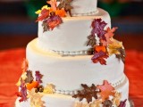 a fall wedding cake decorated with bright sugar leaves and pumpkins and a shiny pumpkin topper