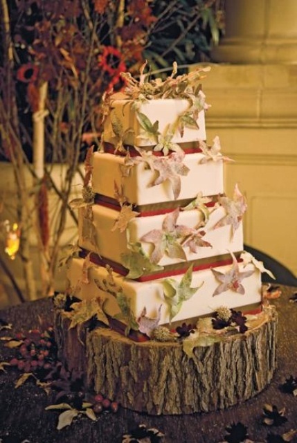 a large square fall wedding cake with burgundy and green ribbons and fall leaf decor all over the cake