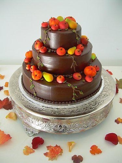 a chocolate wedding cake topped with sugar apples and pears in bright fall colors