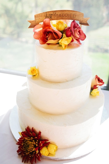 a white fall wedding cake decorated with bright fall leaves and a wooden topper for a stylish look